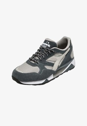 Scarpe sportive con tomaia in mesh grigia e nera, dettagli in camoscio, colletto imbottito, lacci piatti e suola in gomma texturizzata.