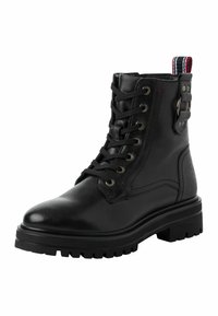 Stivaletto in pelle nera alla caviglia con punta rotonda, chiusura con lacci, occhielli in argento e linguetta a contrasto con righe rosse e bianche. Suola spessa.