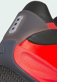 Red and black athletic shoe with textured surfaces, rubber sole, and a translucent heel counter. Features stitching and design accents.