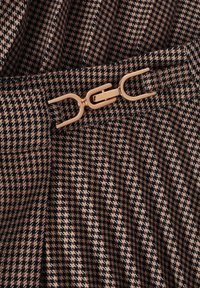 Pruun houndstooth kangas mustade ja roosade aktsentidega, millel on kuldne metallist klamber detail vöökoht. Struktuurne kudumine.
