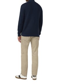 Marineblauer Strickpullover mit hohem Kragen, kombiniert mit beigen Cordhosen. Weiße Sneaker mit schwarzen Akzenten runden den Look ab.
