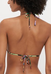 Bikini top with a black base, multicolored tropical pattern, thin straps, and a tie closure at the back. Smooth fabric texture.