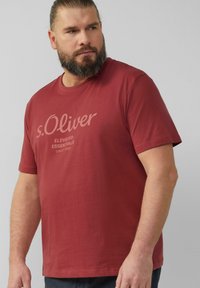 Camiseta de algodón roja con el logo "s.Oliver" en blanco, diseño de cuello redondo, mangas cortas y textura de corte relajado.