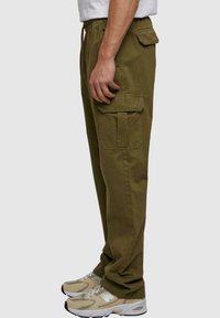 Olivengrønne cargo bukser med elastisk talje, sidelommer og baglommer samt et afslappet fit. Kombineret med beige løbesko.
