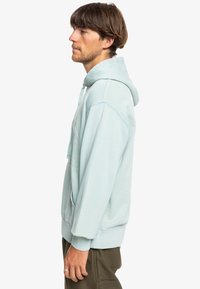 Light blue hoodie with a front pocket and adjustable drawstring. Soft fabric, ribbed cuffs, and hem enhance comfort and fit.