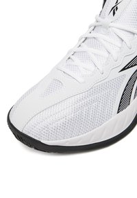 Weißer Sportschuh mit Obermaterial aus Mesh, schwarzer Gummisohle und schwarzen Akzentstreifen. Mit Schnürdesign und strukturierter Oberfläche an den Seiten.