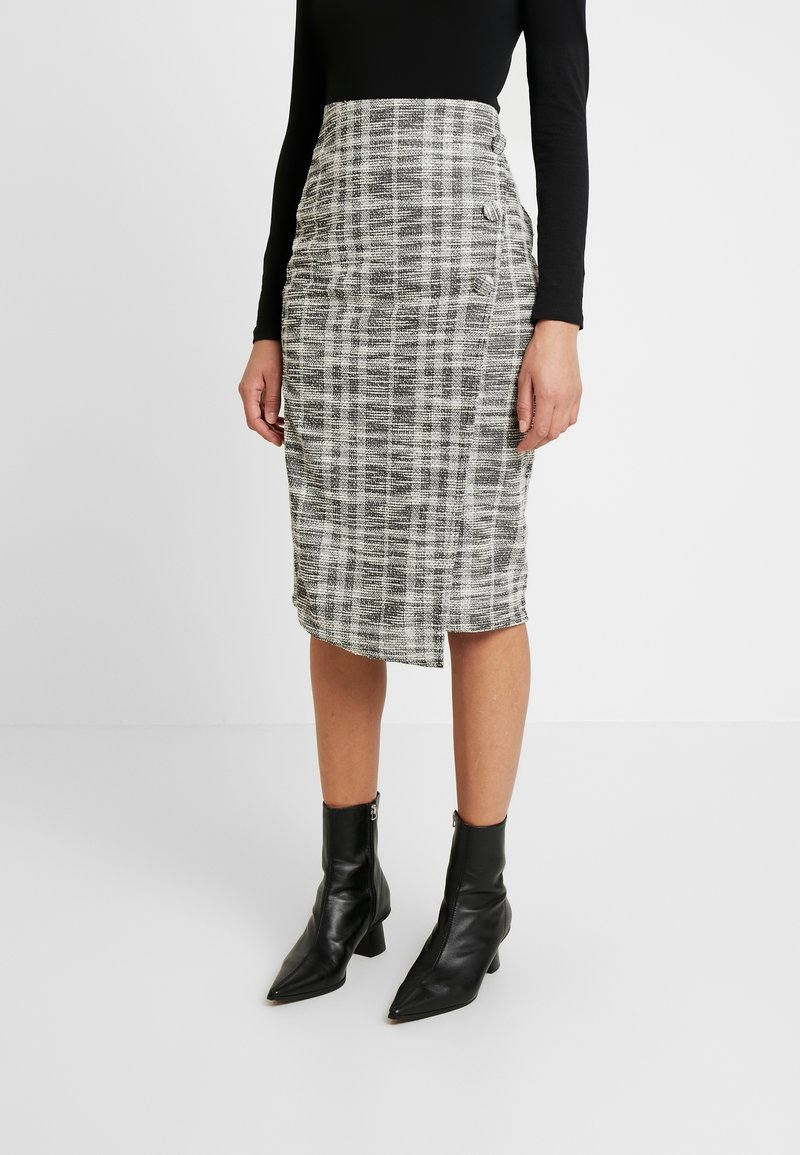 Svart och vit rutigt blyertkjol med en sidofåra, texturerad tyg och knappdetaljer, matchad med svarta ankelstövlar.