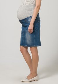 Džínová těhotenská sukně se pružným šedým pasem, s vypasovaným střihem a délkou do kolen. Světlé zesvětlení a klasický pětikapsový styl.