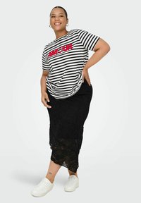 Falda de encaje negra con patrón floral y detalles translúcidos, combinada con una camiseta de rayas blanca y negra con "AMOUR" en texto rojo. Zapatillas blancas.