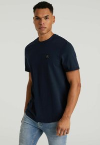 Tumedast sinise värvi lühikeste varrukatega T-särk, mis on valmistatud pehmest kangast, ümarate kaelusega ja väikese musta logoplaastriga rinnal.