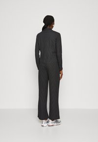 Černé pruhované kalhoty a odpovídající top vyrobené z hladkého, elastického materiálu. Volný střih s rovnými nohavicemi a jemnými detaily.