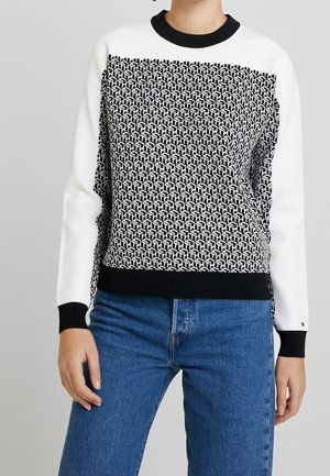 Sweat-shirt à imprimé noir et blanc avec une moitié supérieure blanche unie, des poignets côtelés noirs et une ceinture noire, associé à un jean bleu.
