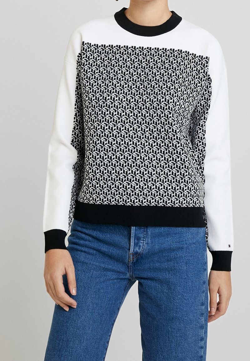 Felpa a motivo bianco e nero con la parte superiore in bianco uniforme, polsini neri a costine e vita nera, abbinata a jeans blu.