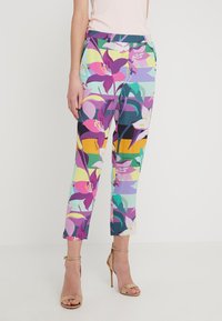 Kolorowe spodnie w kwiatowy wzór w odcieniach fioletu, różu i zieleni. Tkanina ma żywy wzór, dopasowany krój i długość do kostek.