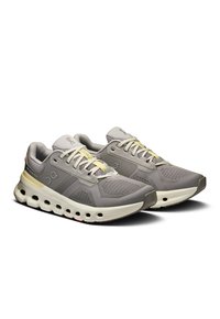 Zapatillas deportivas grises con upper de malla, cordones amarillo claro y una suela blanca gruesa con recortes circulares. Logo en el costado.
