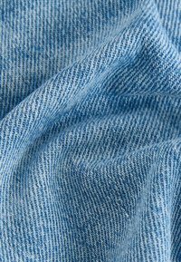 Gros plan sur un tissu en denim bleu clair avec une texture de tissage diagonal visible et des plis doux.