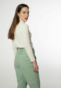Rippierter, langärmliger Rollkragenpullover in Off-White; hoch taillierte, hellgrüne Hose mit strukturiertem Bund und seitlichen Taschen.