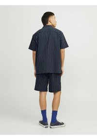 Trumpa rankovė, tamsiai mėlynos juostelės marškiniai ir atitinkamos šortai. Medvilnės medžiaga, laisvas pjūvis, subtili tekstūra su raštu, derinama su mėlynomis kojinėmis ir sportiniais batais.