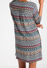 Färgglad tunika med geometriska mönster i rött, blått, grönt och orange. Har trekvartslånga ärmar och en rundad nederkant. Tillverkad av lättviktig tyg.