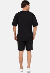 T-shirt noir en coton à manches courtes associé à un short noir, avec une coupe décontractée, un col rond et une texture unie. Des baskets blanches complètent le look.