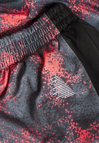 Svarta och röda mönstrade shorts med en elastisk midja, med en färgsplash-design och en liten vit logotyp nära fållen.