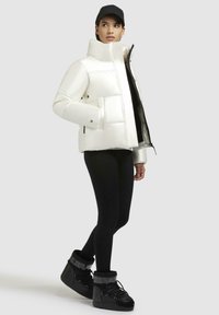 Giacca piumino bianca con colletto alto, chiusura a zip frontale e tasche laterali. Abbinata a leggings neri e stivali neri con lacci.