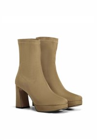 Bottines beiges à la texture lisse et mate, à bout carré et à talon épais. Coutures visibles sur la tige.