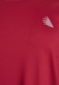 Punainen lyhythihainen t-paita, joka on valmistettu sileästä kankaasta ja jossa on vasemmassa rintataskussa valkoinen, abstrakti kolmion grafiikka.