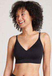 Svart bralette i mjukt tyg, med en djup V-ringning, tunna justerbara band och en sömlös design. Ingen synlig hårdvara.