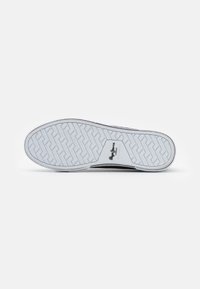 White rubber sole with herringbone pattern and black accents. Logo printed in the center. Smooth texture with a flat profile.