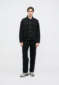 JAQUETA DE DUNKLE EM DENIM com dois bolsos no peito e botões prateados, combinada com calças de denim pretas e ténis cinza. Textura suave, design casual.