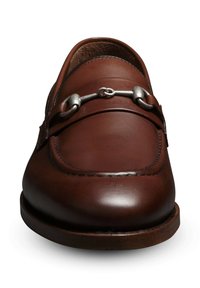 Le mocassin en cuir marron présente un bout arrondi, une finition texturée et un accent en métal argenté sur le dessus du pied. Le design est complété par une semelle en bois.