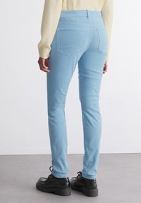 Ljusblå högt skurna jeans med en slät struktur, bakfickor och en medelhög midja, kombinerat med svarta skor. Synliga sömdetaljer.