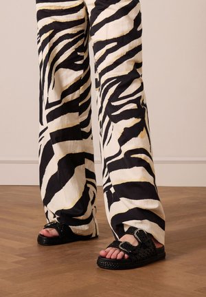 Black and white zebra-patterned wide-leg pants with a lightweight fabric, paired with black woven sandals featuring a buckle accent.