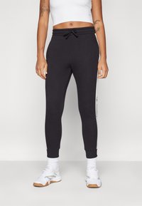 Svarte joggebukser med strikk i midjen, slim fit og hvite sidestreker. Laget av myk tekstil, med tettsittende mansjetter og lommer.
