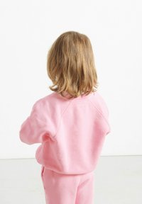 Felpa rosa con vestibilità rilassata, maniche raglan e texture morbida, abbinata a pantaloni rosa coordinati. Vista da dietro.