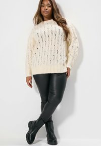 Beige neule, jossa on teksturoitu kuvio, röyhelökaulus ja -helma. Yhdistetty mustiin tekonahkalegginseihin ja mustiin nilkkureihin.