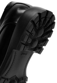 Suola in gomma nera con motivo di grip testurizzato, profilo arrotondato e tallone rinforzato. Bordo superiore liscio con dettagli di cucitura sottili.
