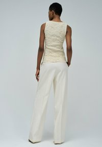 Top de encaje beige sin mangas con un patrón texturizado, combinado con pantalones de pierna ancha de color crema; ambos artículos presentan líneas limpias y un ajuste entallado.