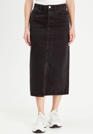 Black denim midi skirt with a front slit, five pockets, and a button closure. Paired with white sneakers for a casual look.