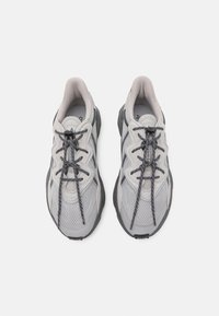 Zapatillas deportivas grises con parte superior de malla y acentos de gamuza, suela texturizada y cordones planos. Diseño ligero con forma curva.