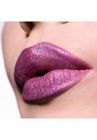Lilla metallisk læbestift på påfyldte læber, med en blank glans og subtil glimmer, der står i kontrast til en naturlig hudfarve baggrund.