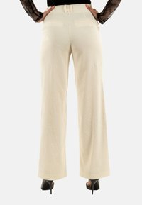 Pantaloni a gamba larga color crema, in tessuto rigato con una texture particolare, cintura elastica e due tasche posteriori, abbinati a tacchi a spillo.