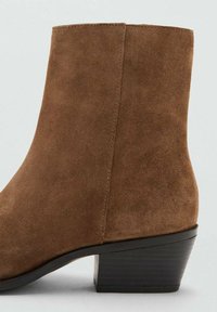 Botín de ante marrón con forma cónica, superficie texturizada y tacón bajo de bloque. Líneas limpias y diseño minimalista.