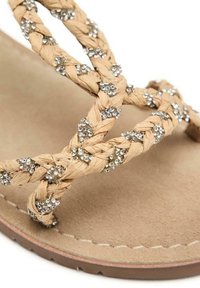 Sandalia plana de tiras trenzadas en color tostado con acentos de cristal, suela plana y plantilla suave en beige. Material texturizado con costuras decorativas a lo largo de los bordes.