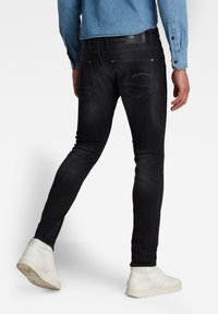 Jeans skiny de mezclilla negra con una textura suave, detalles de costura sutiles y dos bolsillos traseros. Llevados con zapatillas blancas de caña alta.