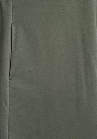 Olivgrön tyg med en slät textur och lätt glans; har en sidoficka med en diskret sömdetalj.