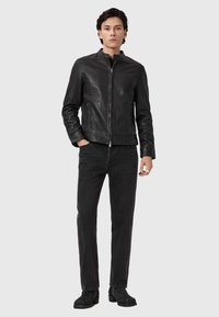 Zwarte leren jas met een hoge kraag, ritssluiting en twee zijzakken, gecombineerd met zwarte denim broek en donkere enkelboots.