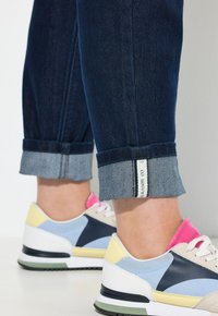 Tmavě modré džíny s ohrnutými nohavicemi a světle modrou podšívkou, doplněné vícero barevnými teniskami s růžovými, modrými a žlutými akcenty.