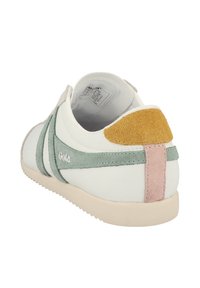 Sneaker bianca con dettagli in suede verde, particolari rosa e gialli, forma arrotondata, suola in gomma testurizzata e logo sul lato.